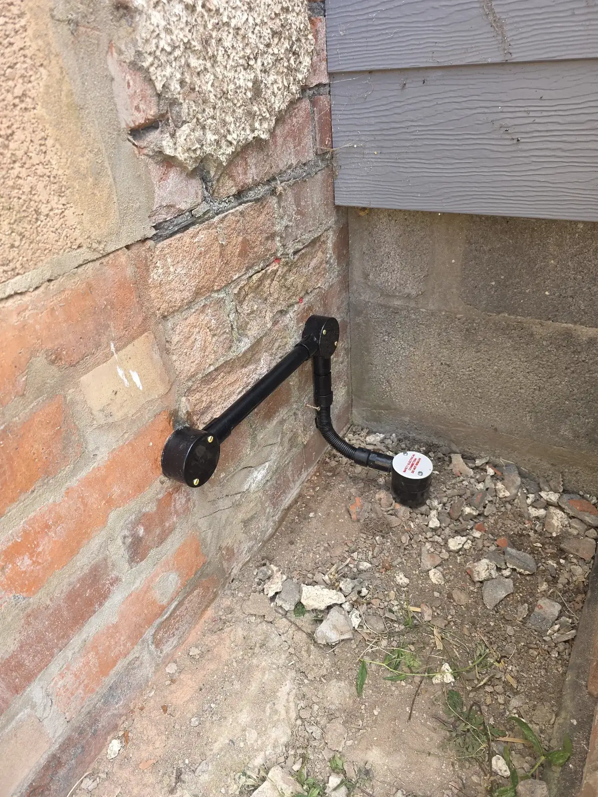 Black conduit on a brick wall running down to a ground-level earth rod pit