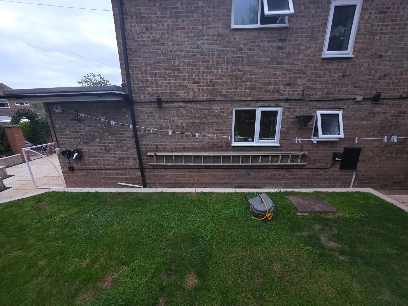 Rear garden view of a house with a new EV charger and supply cable run along the back wall