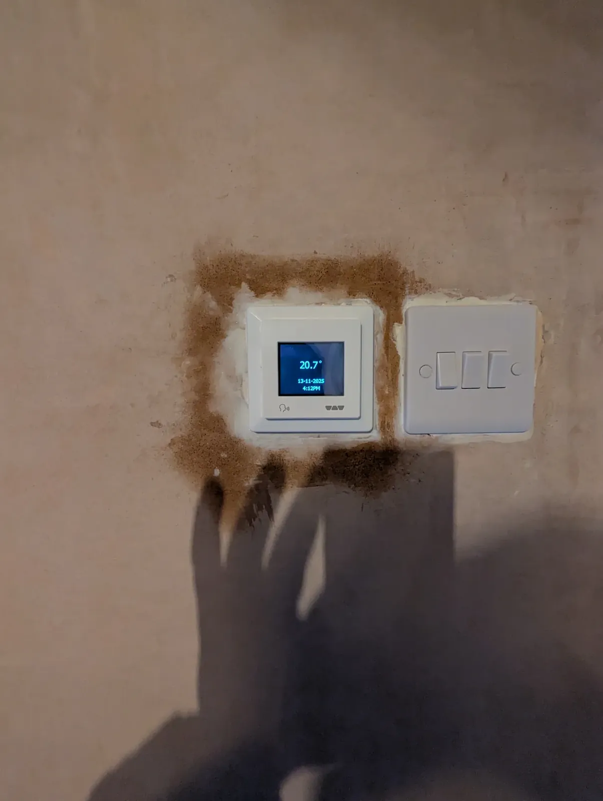 Underfloor heating thermostat and three-gang switch on a freshly filled wall